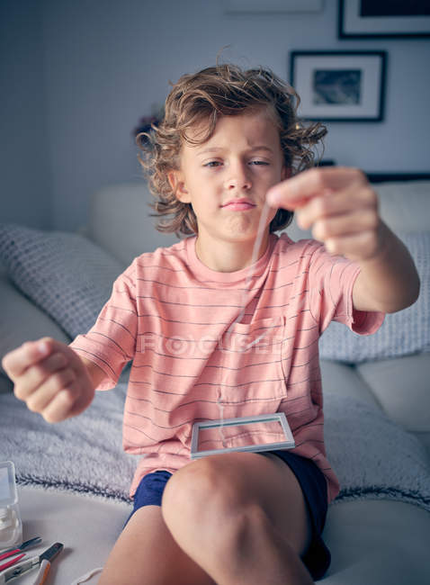 Milk tooth hanging on floss in hands of curly cute kid looking at floss in room — Stock Photo