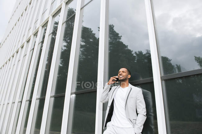Елегантний чорний чоловік говорить смартфон, що спирається на будівлю — стокове фото