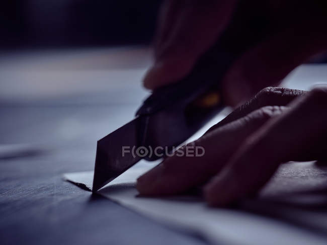 Manos de hombre profesional cortando hojas de papel con cuchillo afilado especial en la mesa de trabajo - foto de stock