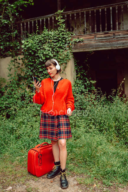 Mujer en auriculares con maleta escuchando música en el campo - foto de stock