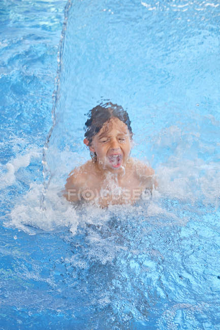 Ребенок с закрытыми глазами и открытым ртом плавает под водопадом в аквапарке — стоковое фото
