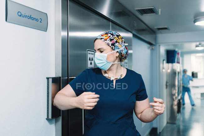 Side view of woman in blue uniform and protective mask coming in operating room and nurse walking along corridor — Stock Photo