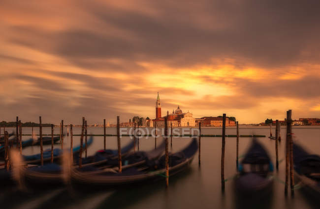 Molo con barche vuote in acqua contro il tramonto ardente e città con vecchie torri e tetti — Foto stock