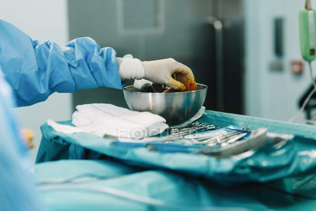 Schnitthand eines Sanitäters in blauem Kleid und weißem Handschuh, der während der Operation einen Tampon voller Jod in eine Schüssel drückt — Stockfoto