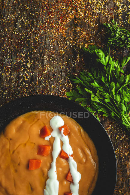 De cima saborosa sopa de creme vegetal perfumado com cenoura madura cortada e salsa em fundo de madeira — Fotografia de Stock