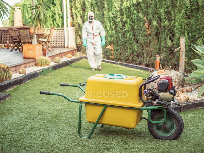 Professional worker in uniform for fumigation walking to equipment on wheel with handle for disinfection — Stock Photo