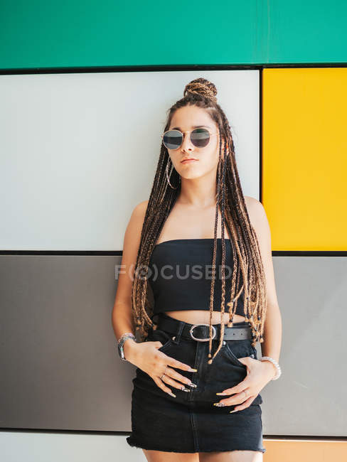 Pretty stylish teenage girl with hands in pockets and unique dreadlocks looking away on colorful background — Stock Photo