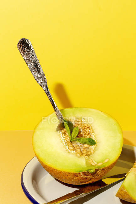 Cut ripe appetizing sweet pitted melon on plate with spoon and fork on yellow background — Stock Photo