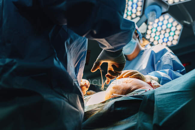 Cirurgião plástico costurando mama de paciente feminina após a inserção de implantes na sala de cirurgia — Fotografia de Stock