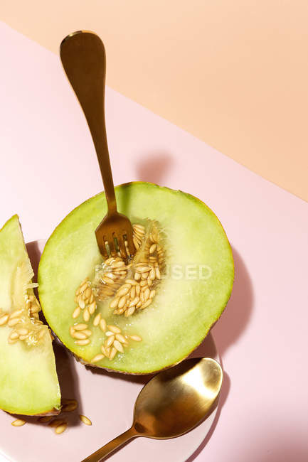 Corte maduro apetitoso doce melão sem caroço com colher e garfo na mesa rosa — Fotografia de Stock