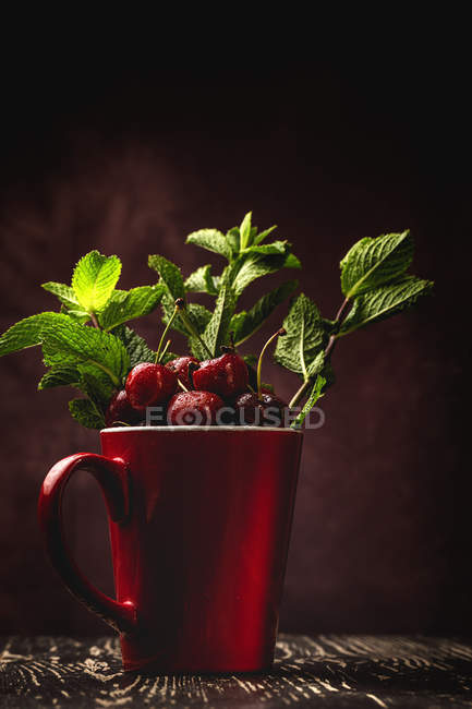Tasty appetizing ripe cherries with leaves in red cup on dark background — Stock Photo
