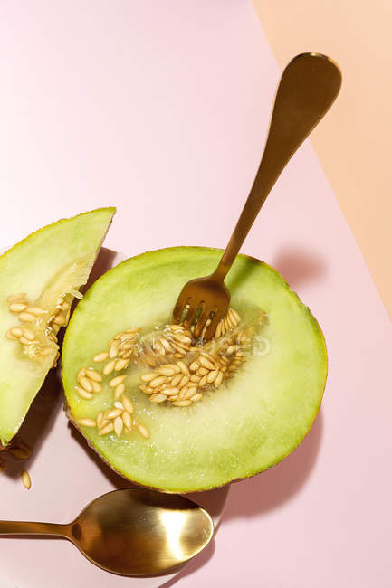 Reife appetitlich süße entkernte Melone mit Löffel und Gabel auf rosa Tisch schneiden — Stockfoto