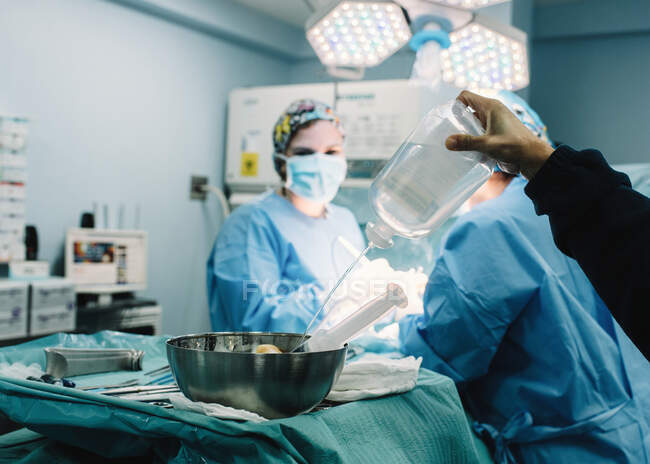 Erntehelfer gießen Kochsalzlösung in Schüssel mit Spritze, während Ärzte im Operationssaal operieren — Stockfoto