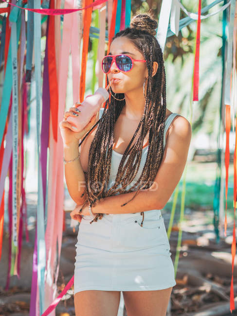 Elegante jovem mulher usando óculos de sol bebendo coquetel durante o festival exterior e olhando para a câmera — Fotografia de Stock
