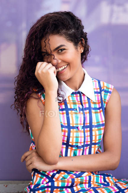Portrait of charming young ethnic young woman with curly hair laughing near purple glass wall — Stock Photo