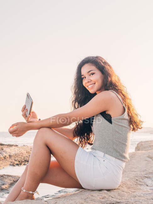 Soñadora mujer joven de moda mensajes de texto en la playa - foto de stock