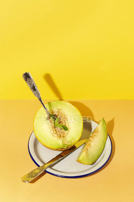Corte maduro apetecível doce melão sem caroço no prato com colher e garfo no fundo amarelo e laranja — Fotografia de Stock