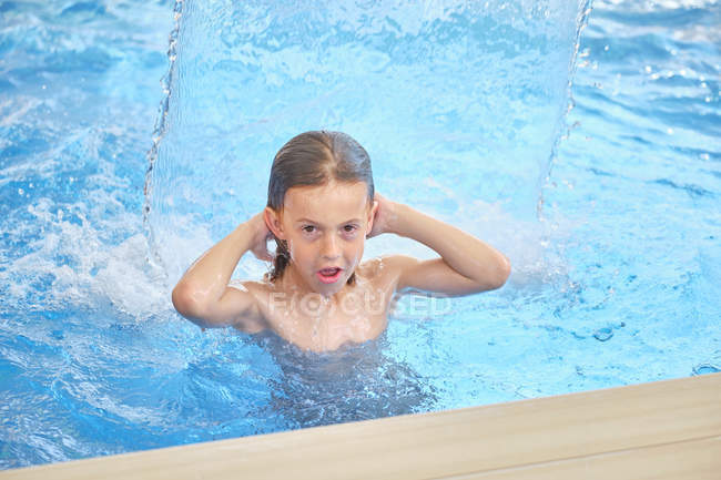 Abrasagem infantil para ar olhando para a câmera e boca aberta enquanto flutuando sob cachoeira no parque aquático — Fotografia de Stock