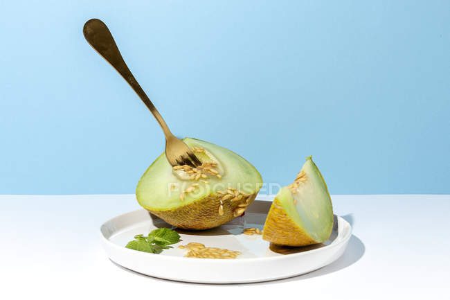 Corte maduro apetitoso melón picado dulce en el plato con cuchara y tenedor sobre fondo azul - foto de stock