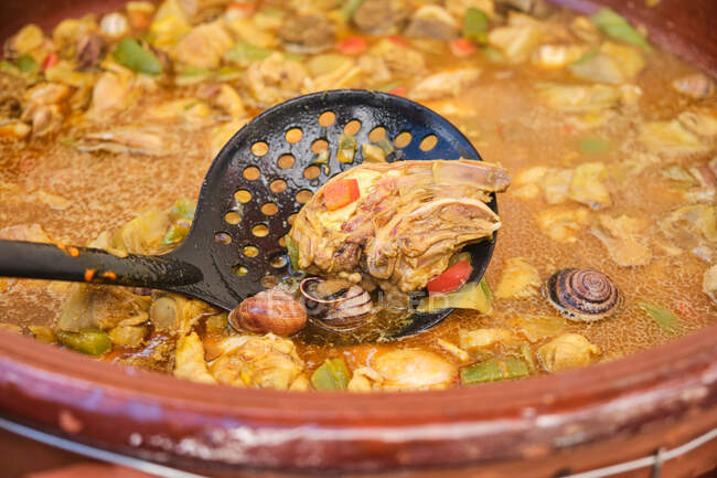 Éplucheur dans une grande casserole en terre cuite avec plat de cuisson de poulet riz assorti légumes et escargots — Photo de stock