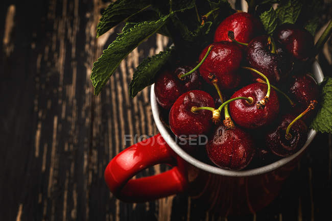 Смачний Апетитний вишня стиглі з листям в червоному стаканчику на темному дерев'яному столі — стокове фото