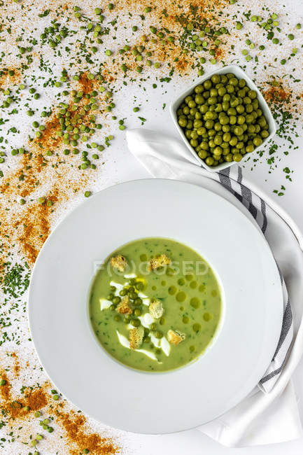 From above mashed vegetable creamy soup with small crackers and green peas in white bowl on wooden background — Stock Photo