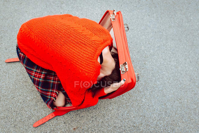 Donna in maglione rosso divertirsi cercando di nascondersi in valigia rossa su strada — Foto stock
