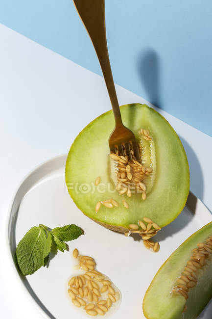 Corte maduro apetitoso melón picado dulce en plato con tenedor en fondo azul y blanco - foto de stock