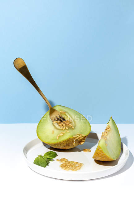 Corte maduro apetitoso doce melão sem caroço na placa com garfo em fundo azul e branco — Fotografia de Stock