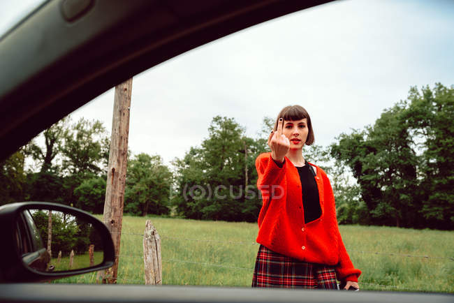 Jeune femme en pull rouge gesticulant près de la voiture sur la route — Photo de stock