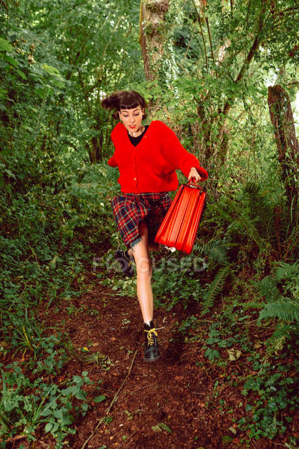 Donna in rosso con grande valigia vintage in esecuzione nel bosco verde — Foto stock