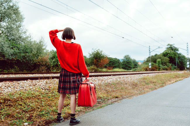 Mujer con maleta caminando por las corbatas del ferrocarril y mirando a la distancia - foto de stock