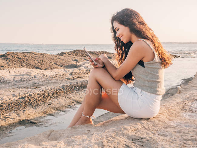 Мрійлива модна молода жінка смс на пляжі — стокове фото