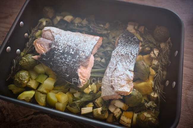 From above roasting pan with large pieces of salmon with skin on garnish of assorted baked vegetables and greens — Stock Photo
