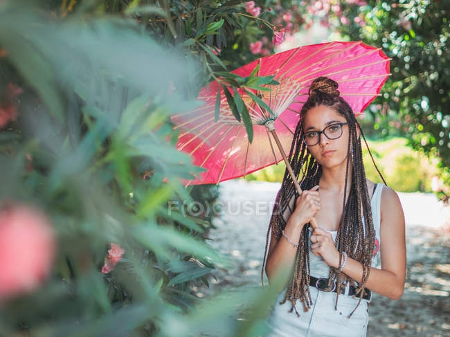 Pensive young woman in summer outfit with umbrella standing in park — Stock Photo
