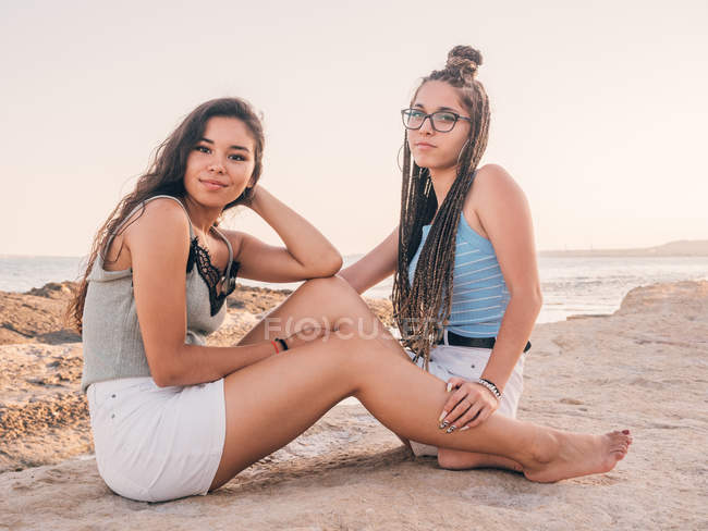 Delighted happy casual female friends sitting on summer beach at sunset — Stock Photo