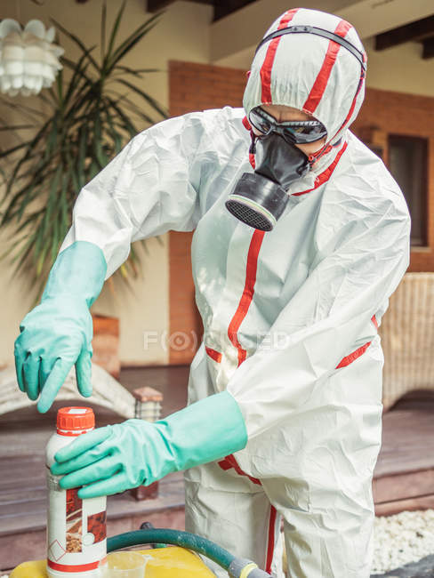 Человек в костюме для дезинфекции, наливающий химикат в бак — стоковое фото
