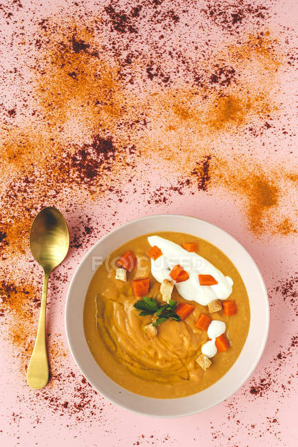 From above tasty aromatic orange vegetable cream soup with sliced carrot and parsley in white bowl on pink background — Stock Photo
