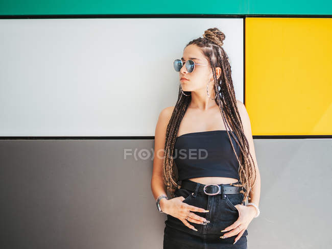 Стильная девушка подросток с уникальными дредами глядя в сторону на красочном фоне — стоковое фото