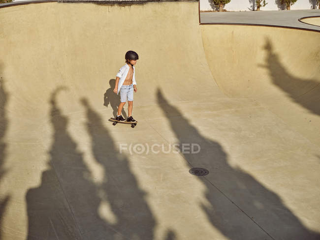 Зверху щасливий маленький хлопчик в захисному шоломі і їзда скейтборд на пандусі в скейтпарку — стокове фото