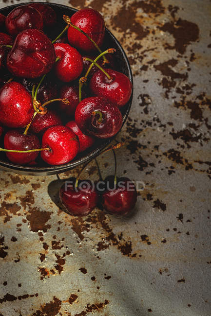Leckere reife Kirschen in Schüssel auf rostiger Tischplatte — Stockfoto