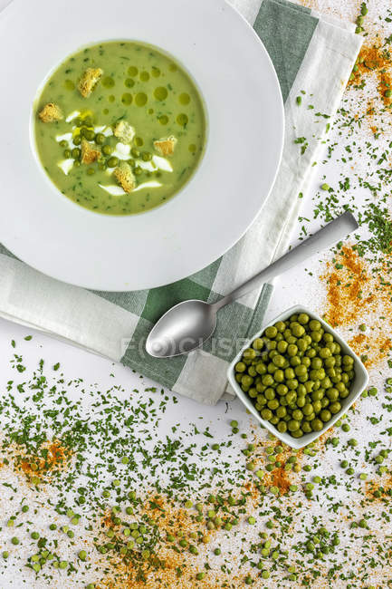 From above mashed vegetable creamy soup with small crackers and green peas in white bowl on wooden background — Stock Photo