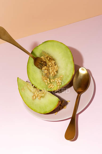 Cut ripe appetizing sweet pitted melon on plate with spoon and fork on pink background — Stock Photo