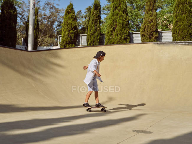 Happy little boy wearing protective helmet and riding skateboard on ramp in skatepark — Stock Photo