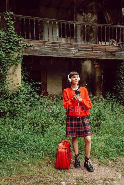 Жінка в навушниках з валізою слухає музику в сільській місцевості — стокове фото