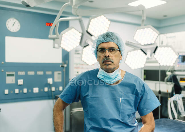 Uomo adulto in uniforme medica in piedi nella moderna sala operatoria durante il lavoro in ospedale — Foto stock