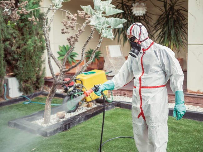 Fumigateur en blanc uniforme pulvérisation substance sur le jardin — Photo de stock