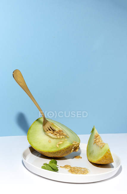 Corte maduro apetitoso doce melão sem caroço na placa com garfo em fundo azul e branco — Fotografia de Stock