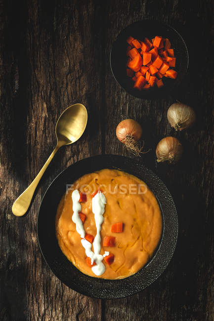 D'en haut une savoureuse soupe parfumée à la crème aux légumes avec des carottes et des oignons sur fond de bois. — Photo de stock