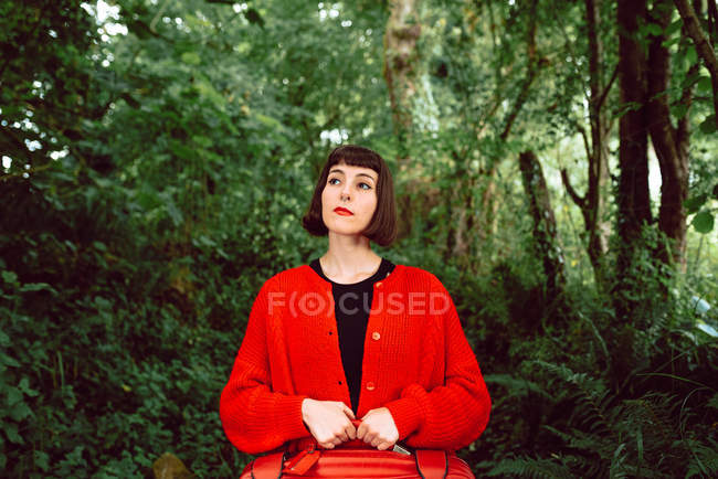 Жінка в червоному з червоною валізою, що йде в зеленому лісі — стокове фото